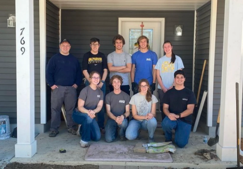 A group of nine people, including members of the American Society of Civil Engineers, pose and smile together on the porch of a house under construction.